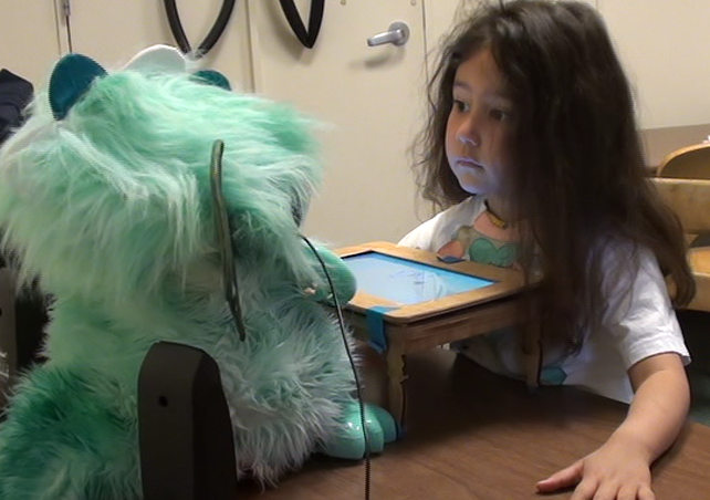 a girl sits across from a dragon robot at a small play table