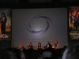 _a panel of five women sitting on a stage in front of a projector screen_