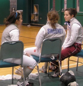 three VC women's foilists sitting in green chairs, backs to the camera