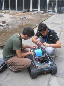 two men crouching over a boxy robot