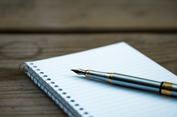 a fancy pen resting on a lined spiral bound notebook